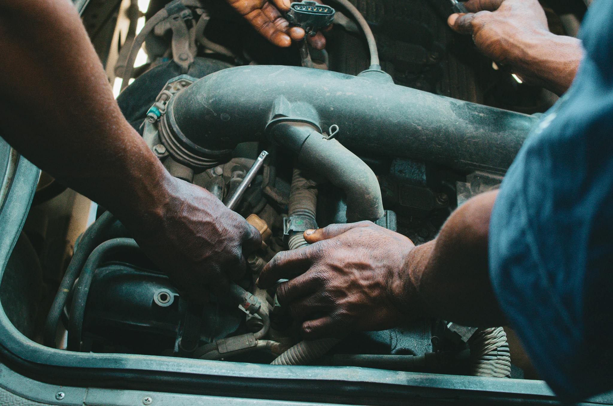 Close-up of mechanics working on a vehicle engine, showing teamwork and precision in car maintenance.